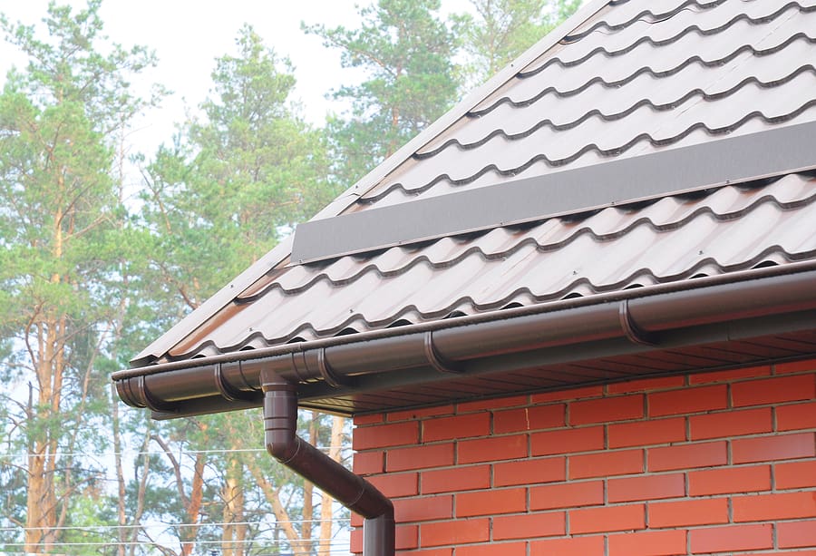 A close-up view of a house with a modern metal roof and brick exterior, showcasing well-maintained gutters. The image highlights the effectiveness of roof waterproofing and proper drainage systems.