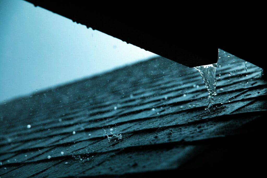 
A close-up shot of a roof during heavy rain, highlighting water flowing off the edge. The image emphasizes the importance of roof waterproofing to prevent water damage.