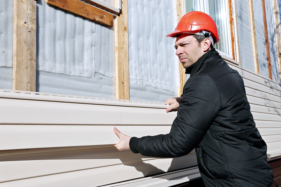 Construction worker in a red hard hat installing beige vinyl siding on a home, demonstrating professional siding replacement by Wagner. This installation showcases the durable materials and expert craftsmanship that enhance a home's exterior, improving both curb appeal and weather resistance.