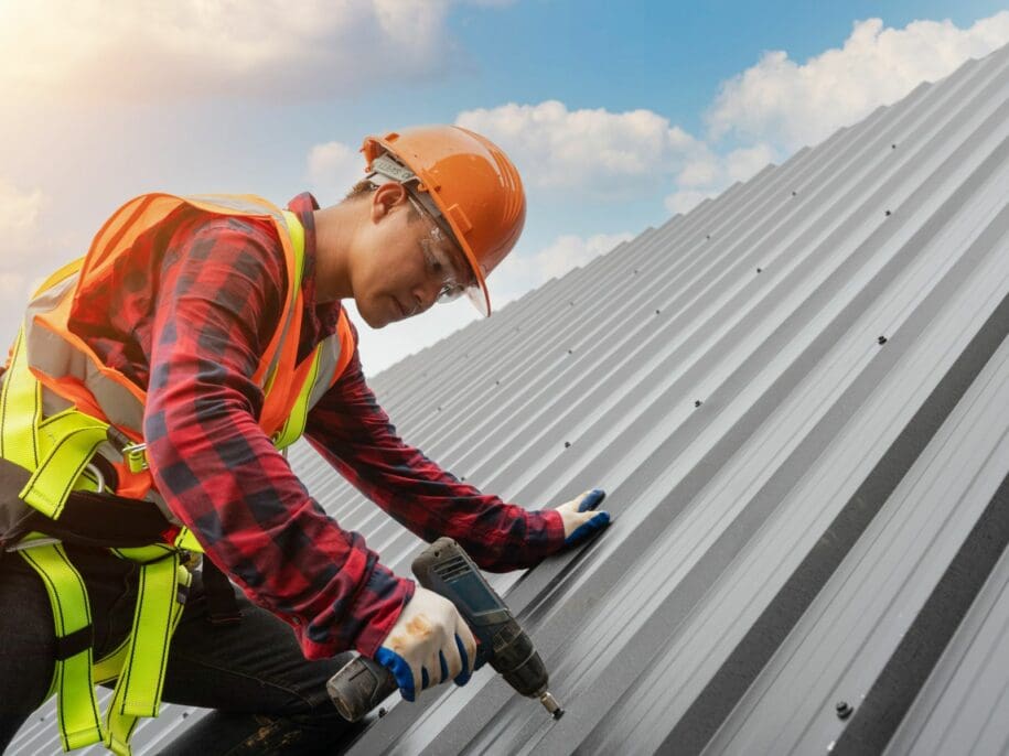 Roofing contractor installing metal roofing panels with power drill during professional roof installation by Wagner Roofing